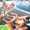 Group of friends relaxing on a boat's netted deck under the sun.
